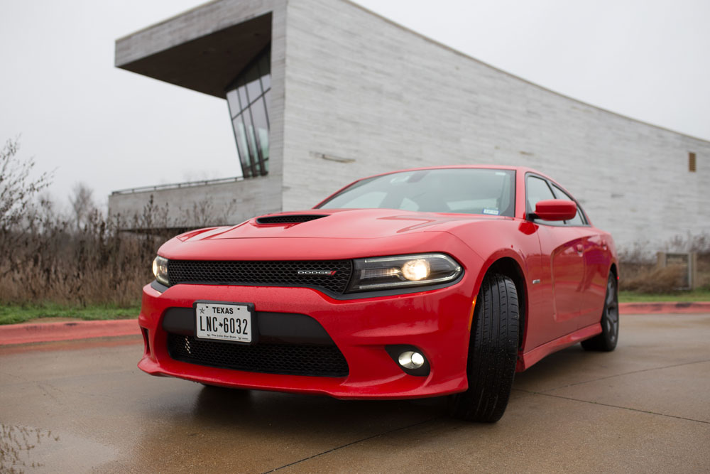 A red Dodge car in front of a long, grey, modern-design building